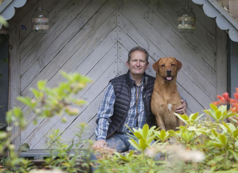 Man sitting in a garden with his pet labrador.